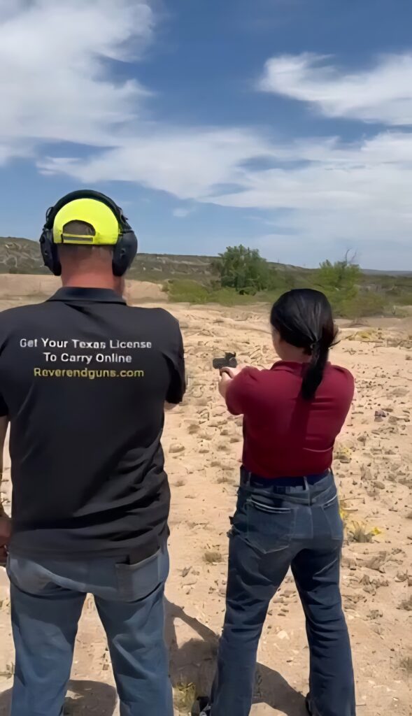 A woman aims a handgun at a shooting range while receiving instruction from a man beside her. The scene highlights firearm training and safety.