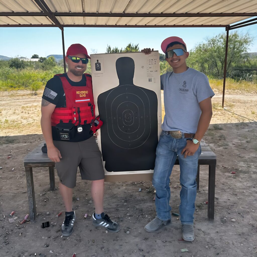 Two men stand beside a shooting target on a range, smiling. The target shows bullet impacts, highlighting their firearm training session.